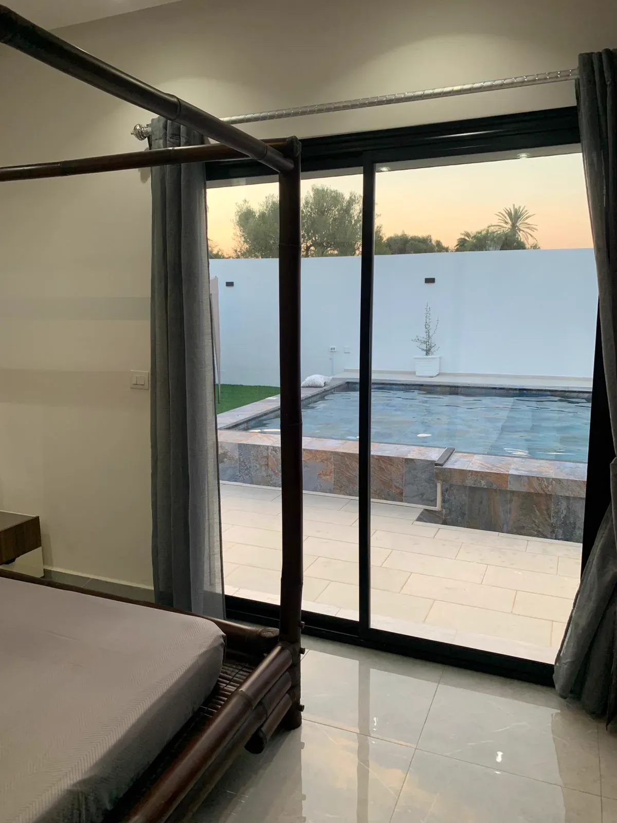 Suite parentale avec lit baldaquin en bambou et vue sur la piscine au coucher du soleil